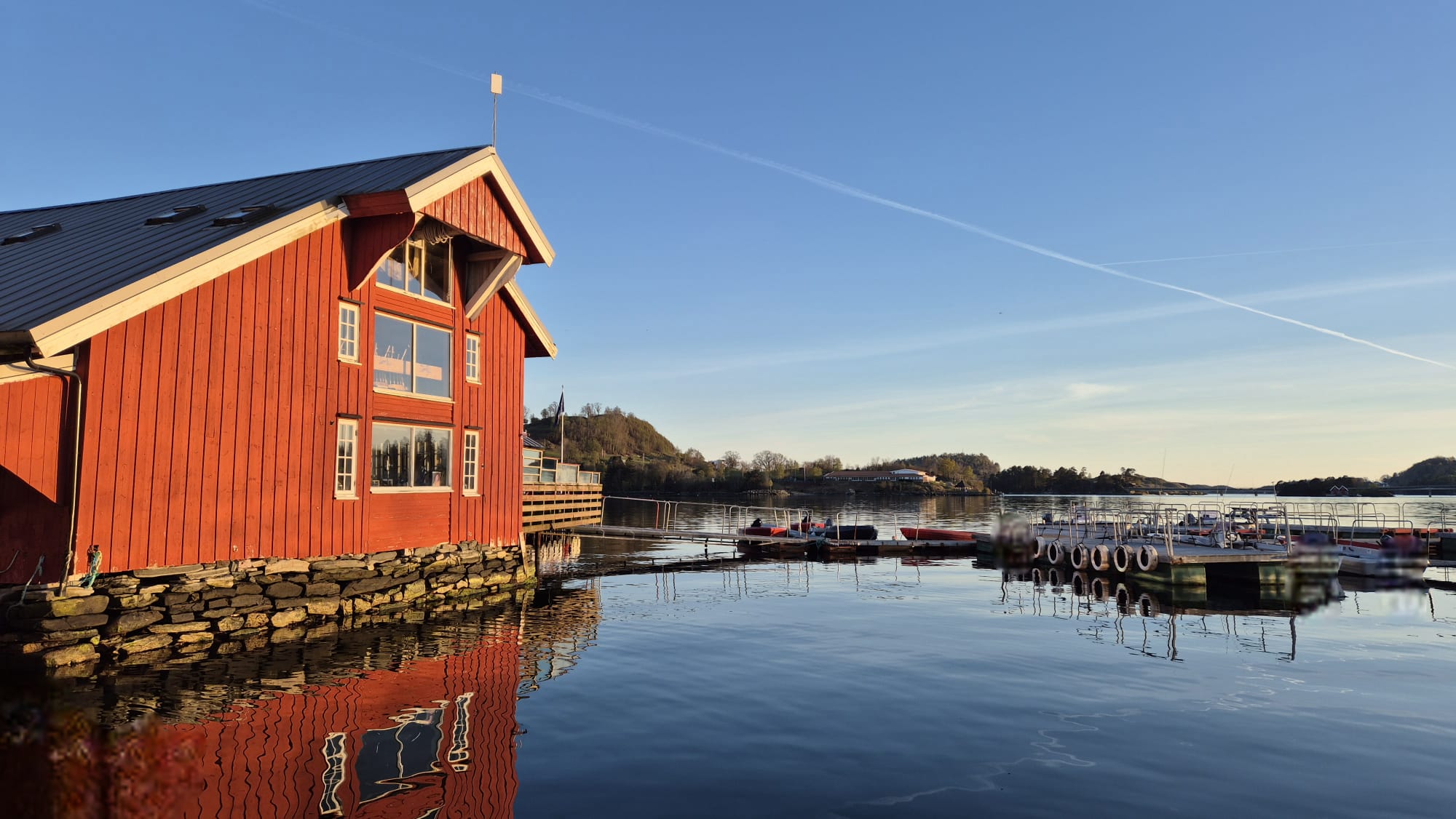 Rødt sjøhus og brygge i kveldslys